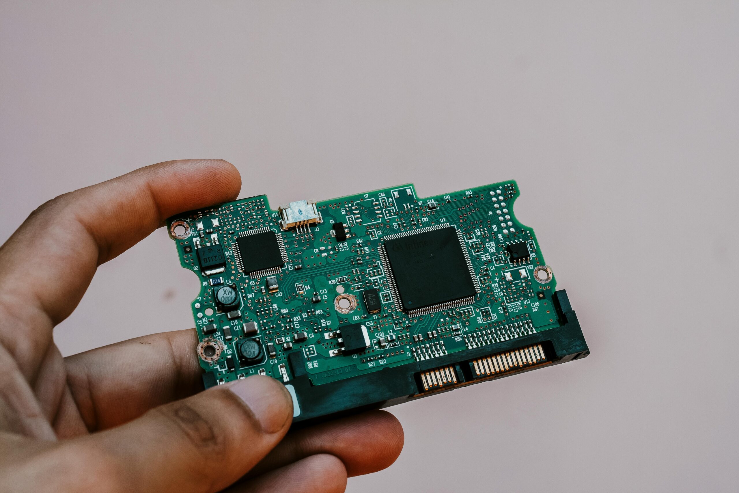 Close-up image of a hand holding a circuit board from a hard drive, showcasing electronic technology.